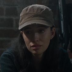 a woman wearing a hat sitting in front of a brick wall