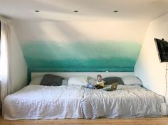 a child is sitting on a bed in front of a wall with green and blue paint