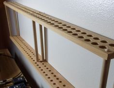 a wooden shelf with holes on the bottom and two pegs attached to it in front of a white wall