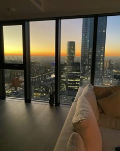 a living room filled with furniture and large windows overlooking the city at sunset or dawn