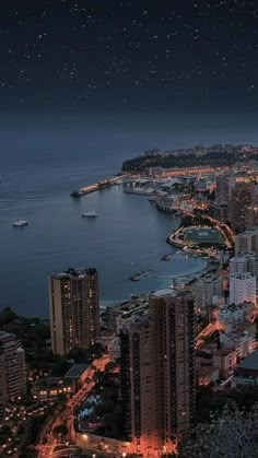 an aerial view of a city at night with the ocean in the foreground and boats on the water