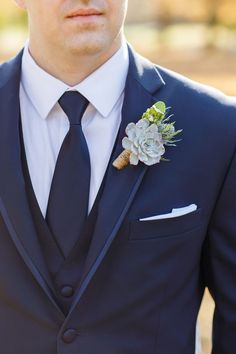 a man wearing a suit and tie with a succulent boutonniere on his lapel