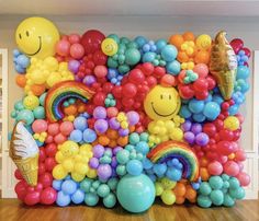 a large balloon wall with smiley faces and rainbow balloons on the top, along with other balloons