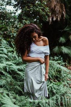 a woman standing in ferns with her arms around her waist and looking down at the ground