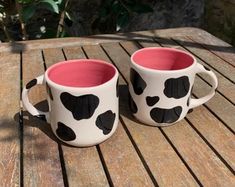 two coffee mugs with black and white spots on them sitting on a wooden table