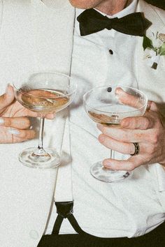 a man in a tuxedo holding two wine glasses