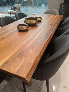 a wooden table with two bowls on it in front of some black chairs and windows