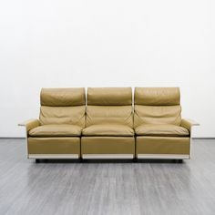 a tan leather couch sitting on top of a wooden floor next to a white wall