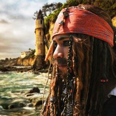 a man with dreadlocks and a red bandana standing in front of the ocean