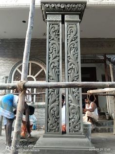 two men are working on an ornately carved clock tower in front of a building