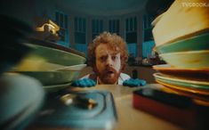 a man sitting at a table with stacks of plates on top of it and looking surprised