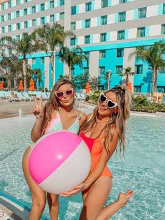 two women in swimsuits standing next to a pool with a large beach ball