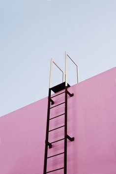 a ladder leaning against a pink wall with a blue sky in the backround