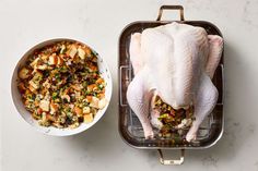 a whole chicken in a pan next to a bowl of stuffing on a white table