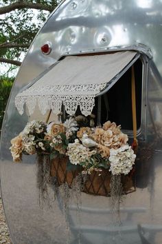 a silver trailer with flowers in it and an awning over the window that is open