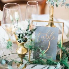 the table is set with gold vases, greenery and a chalkboard sign