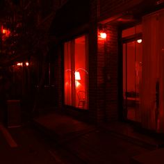 a red light shines in the window of a building at night, with an iron chair sitting outside