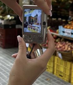 a person holding up a cell phone to take a picture in front of some fruit