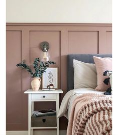 a bedroom with pink walls and a white nightstand next to a bed covered in blankets