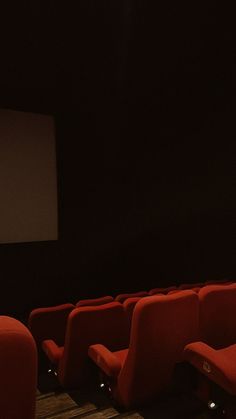 an empty movie theater with red seats and a projector screen in the back ground