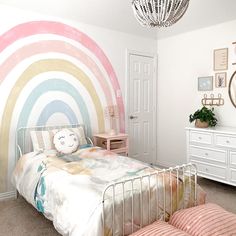 a bedroom decorated in pastel colors with a rainbow painted on the wall