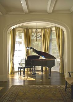 a grand piano sitting in the middle of a living room next to a chandelier