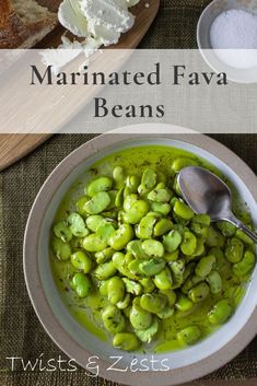 a bowl filled with green beans next to bread and butter on a cutting board that says marinated fava beans