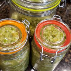 three jars filled with pickles sitting on top of a counter