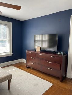 a living room with blue walls and wooden furniture in the corner, along with a large flat screen tv on top of a dresser