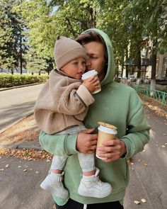 a man holding a small child while wearing a hoodie and drinking from a coffee cup