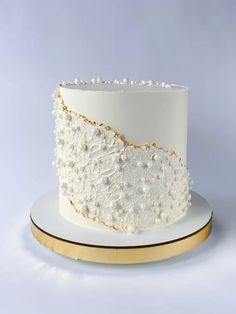 a white and gold wedding cake with pearls on the top is sitting on a plate