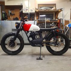 a red and white motorcycle parked inside of a garage next to a metal shelf filled with tools