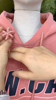 a woman is working on her pink hoodie with an appliqued flower