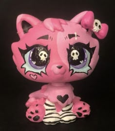 a pink and black cat figurine with skulls on it's head, sitting in