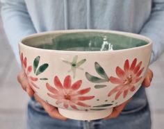 a person holding a bowl with red flowers painted on the side and green leaves in the middle