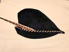 a black hat with feathers on it laying on top of a white bed coverlet