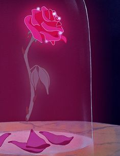 a pink rose in a glass vase on a table with petals scattered around the base