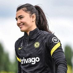 a woman in black and yellow soccer uniform smiling at the camera with her hair pulled back