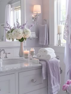 a white bathroom with flowers and towels on the counter top, candles in front of the mirror