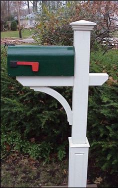 a green and red mailbox sitting on the side of a white post in front of some bushes