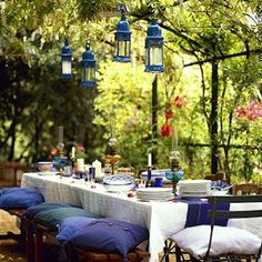 an outdoor dining table with blue lanterns hanging from it's ceiling and plates on the table