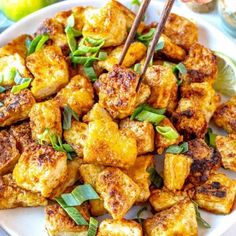 a white plate topped with fried tofu and green onions next to chopsticks