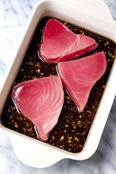 raw fish fillets in a white dish on a marble countertop, ready to be cooked