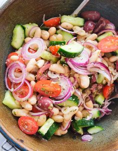 a salad with beans, cucumbers, tomatoes and onions in a brown bowl