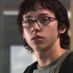 a young man with glasses is looking at the camera while wearing a green shirt and black backpack