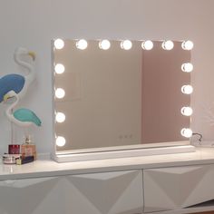 a flamingo is standing in front of a vanity mirror with lights on it and a bird figurine next to it