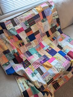 a multicolored patchwork quilt sitting on top of a couch next to a window