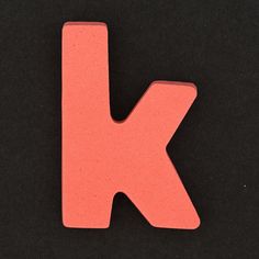 the letter k is made out of pink foam and sits on a black table top