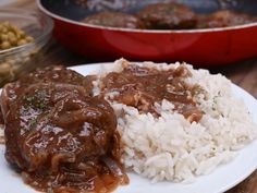 a white plate topped with rice and meat covered in gravy on top of a wooden table