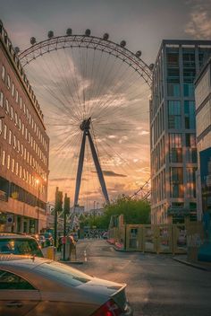 a ferris wheel in the middle of a city street at sunset with cars parked on the side